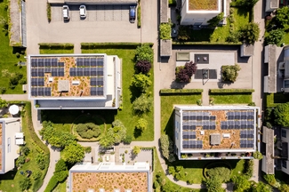 Foto von zwei Häusern in einer Siedlung. Auf dem Flachdach beider Häuser ist eine Solaranlage installiert.